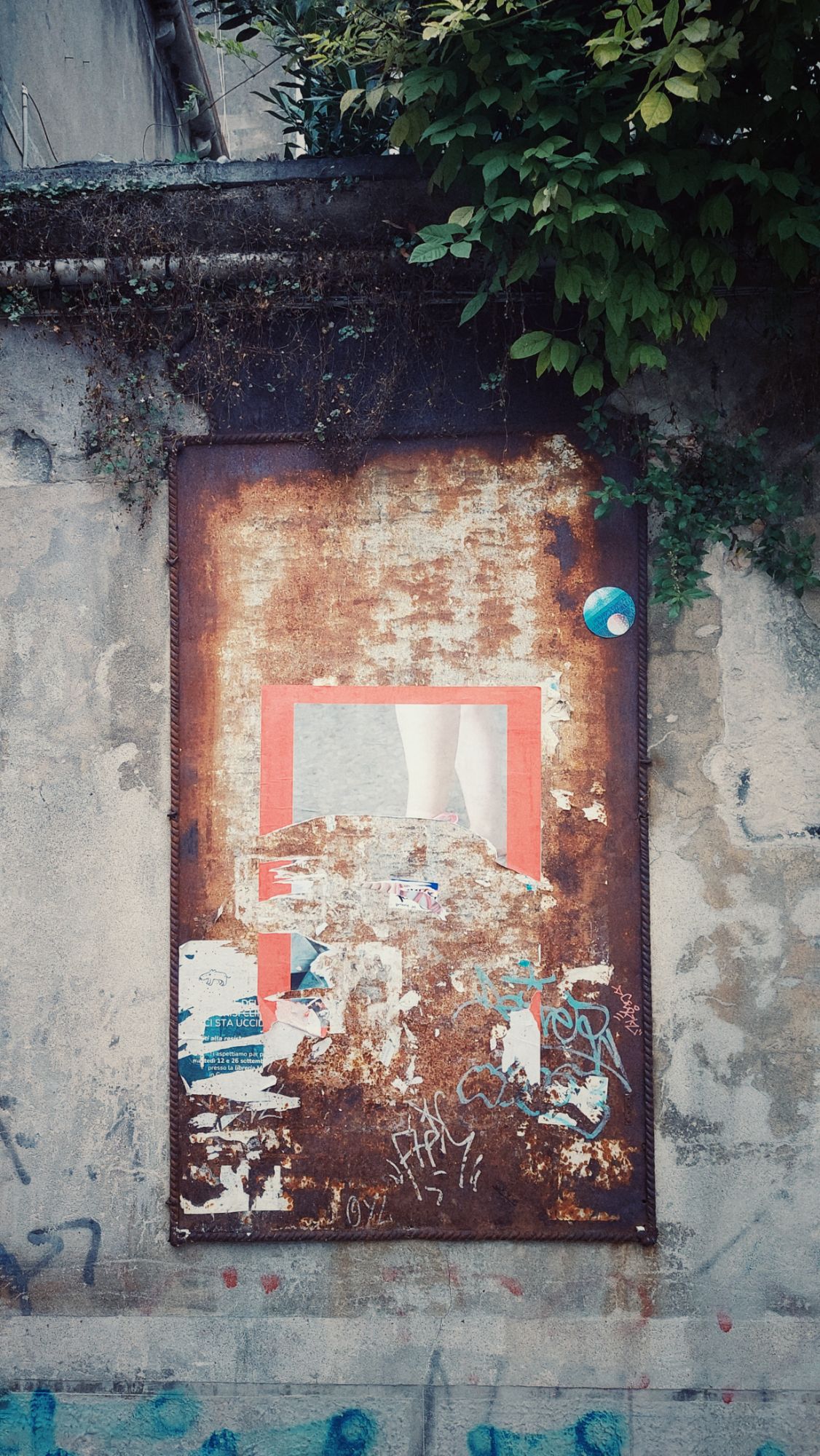 A rusty plate on an old wall. Remainders of old posters still on the surface. 