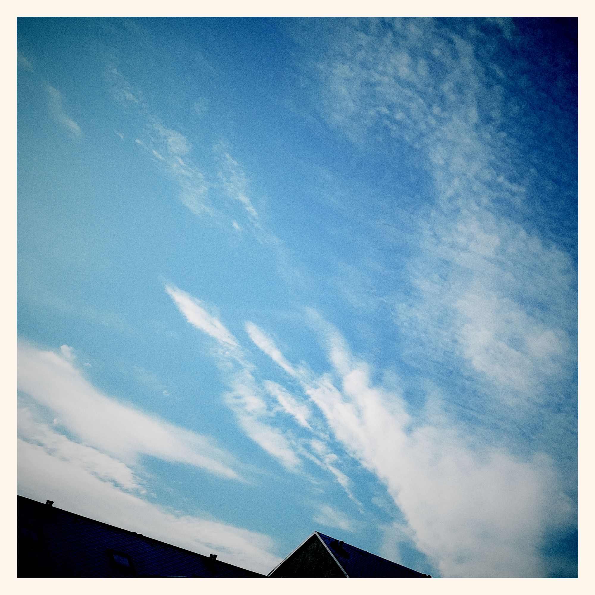 White clouds in a feather-like structure on blue sky. Parts of a roof below.